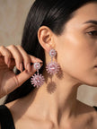 Dark-haired woman wearing pink crystal sunburst drop earrings with a black top against a neutral background