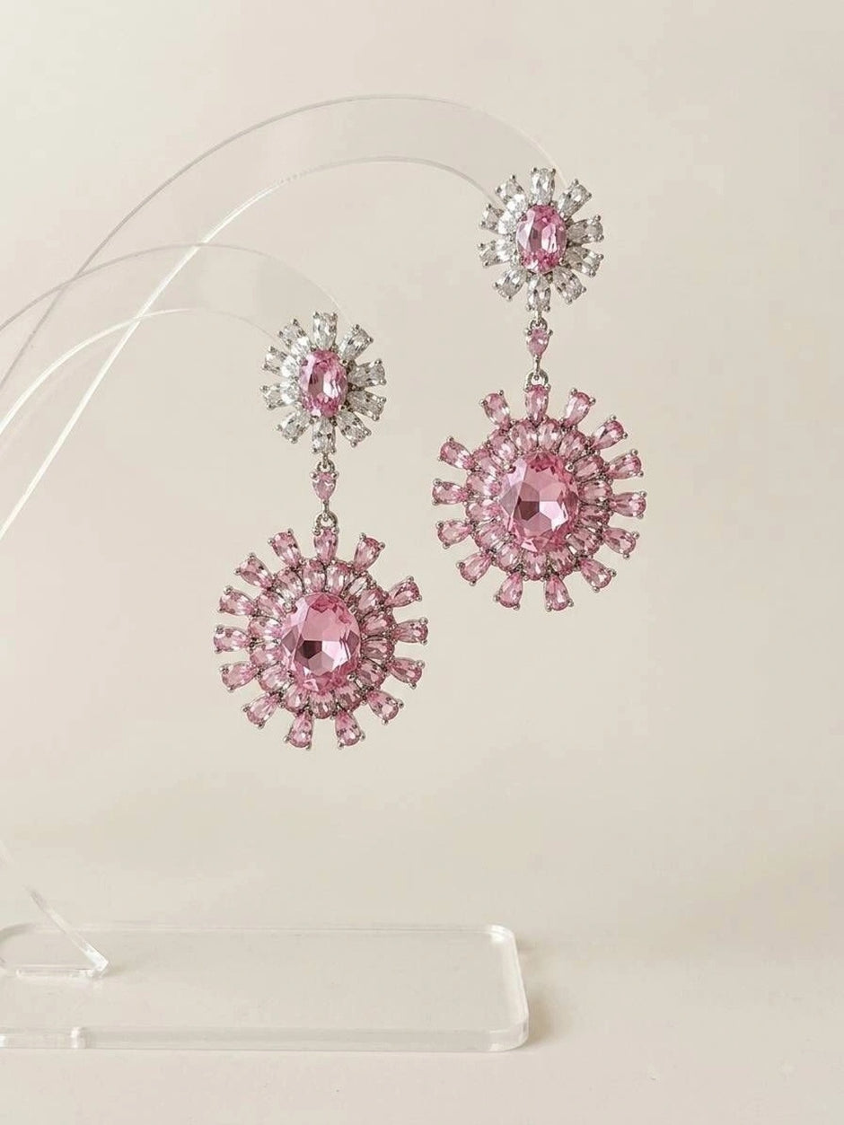 Pair of pink cubic zirconia floral drop earrings displayed on a clear acrylic stand against a light background
