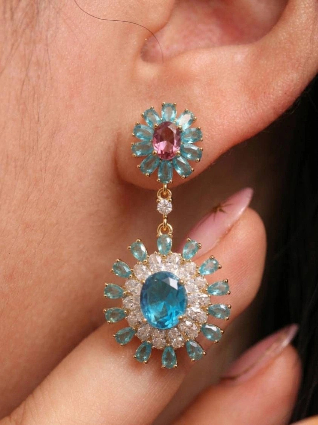Close-up of blue zircon floral drop earring worn on a woman's ear showing full length