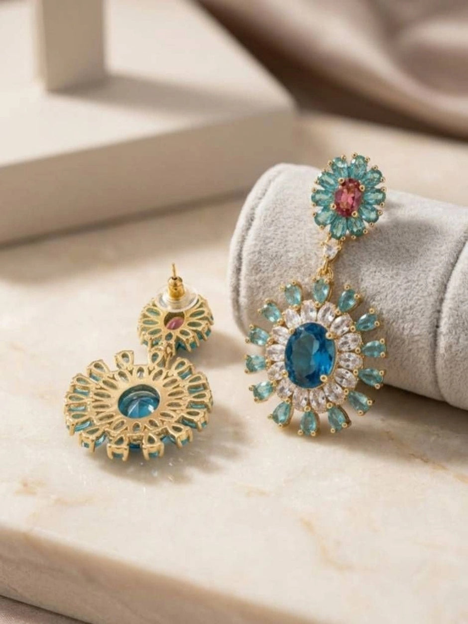 Front and back view of blue zircon drop earrings resting on a grey velvet roll