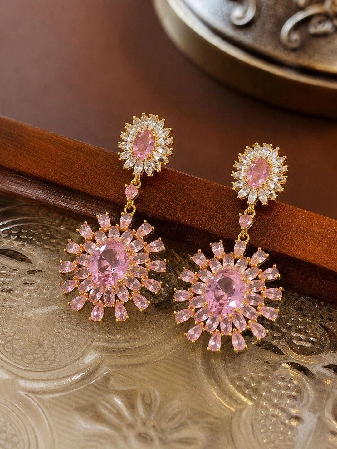 Pair of pink CZ sunburst drop earrings resting on a decorative gold tray