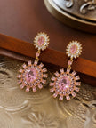 Pair of pink CZ sunburst drop earrings resting on a decorative gold tray