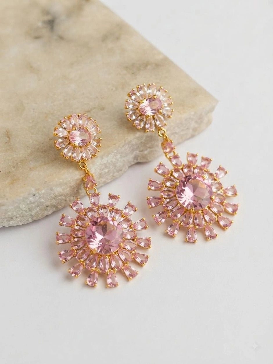 Two pink CZ floral drop earrings displayed on a white stone surface
