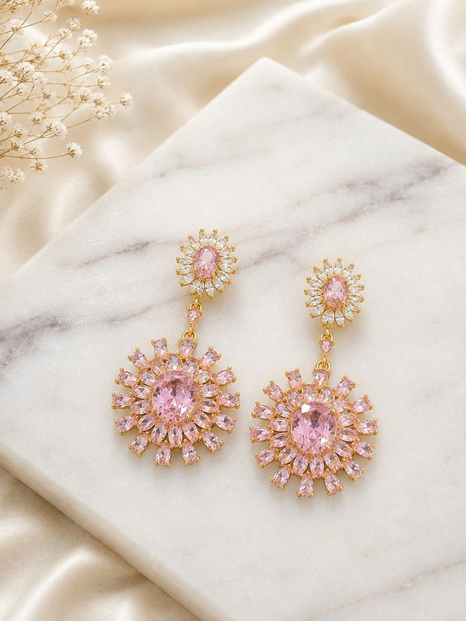 Gold-plated pink CZ floral drop earrings laid flat on a marble surface