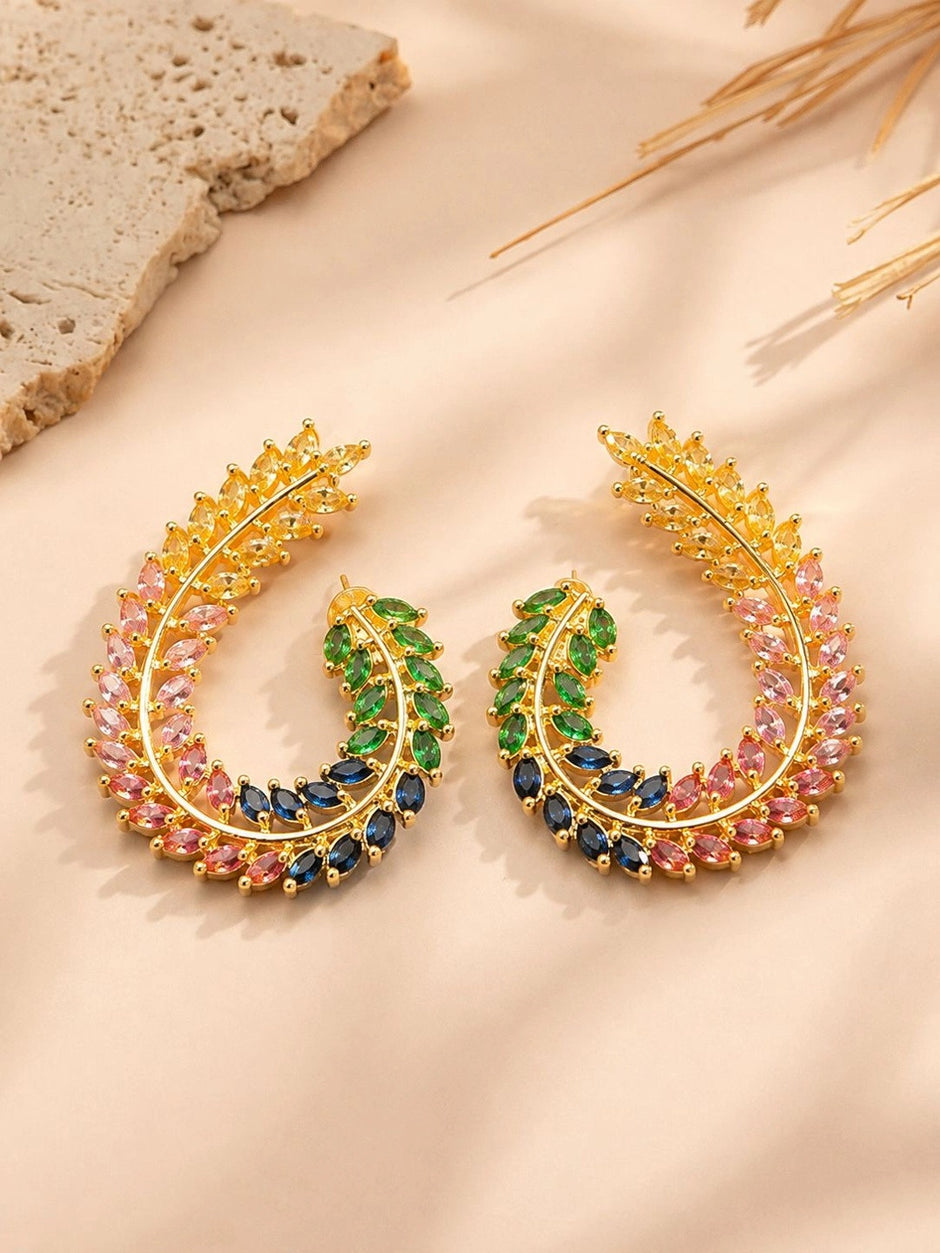 Pair of gold-plated multicolour CZ leaf half-hoop earrings displayed on a beige surface with dried grass stems