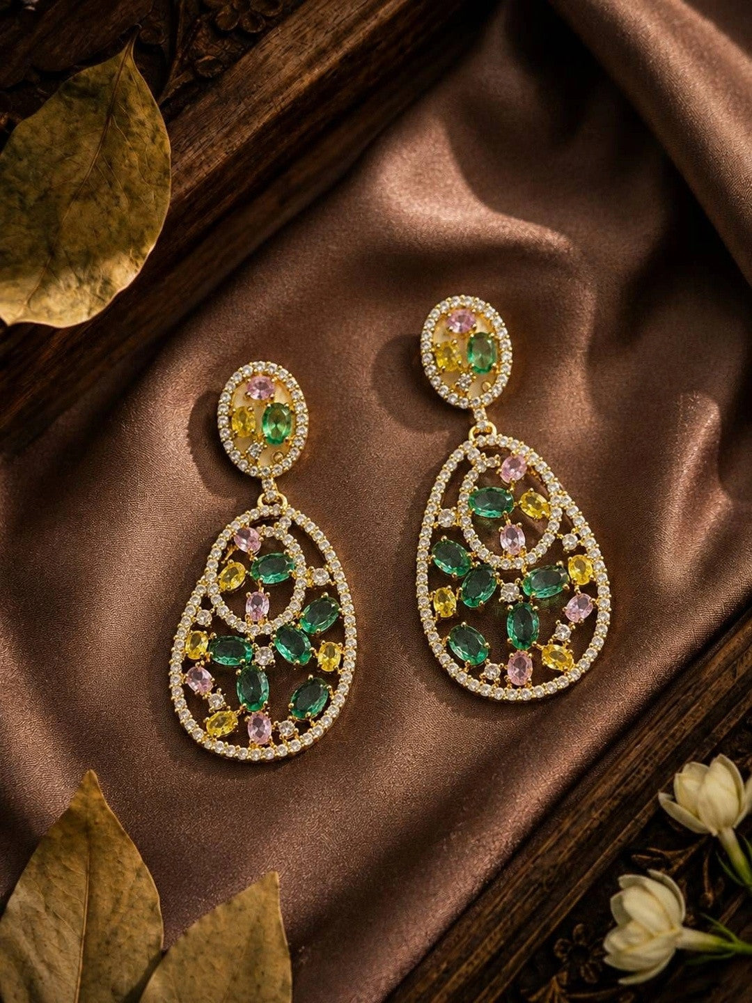 Pair of gold-plated multicolour CZ open teardrop earrings laid on brown satin fabric with flowers