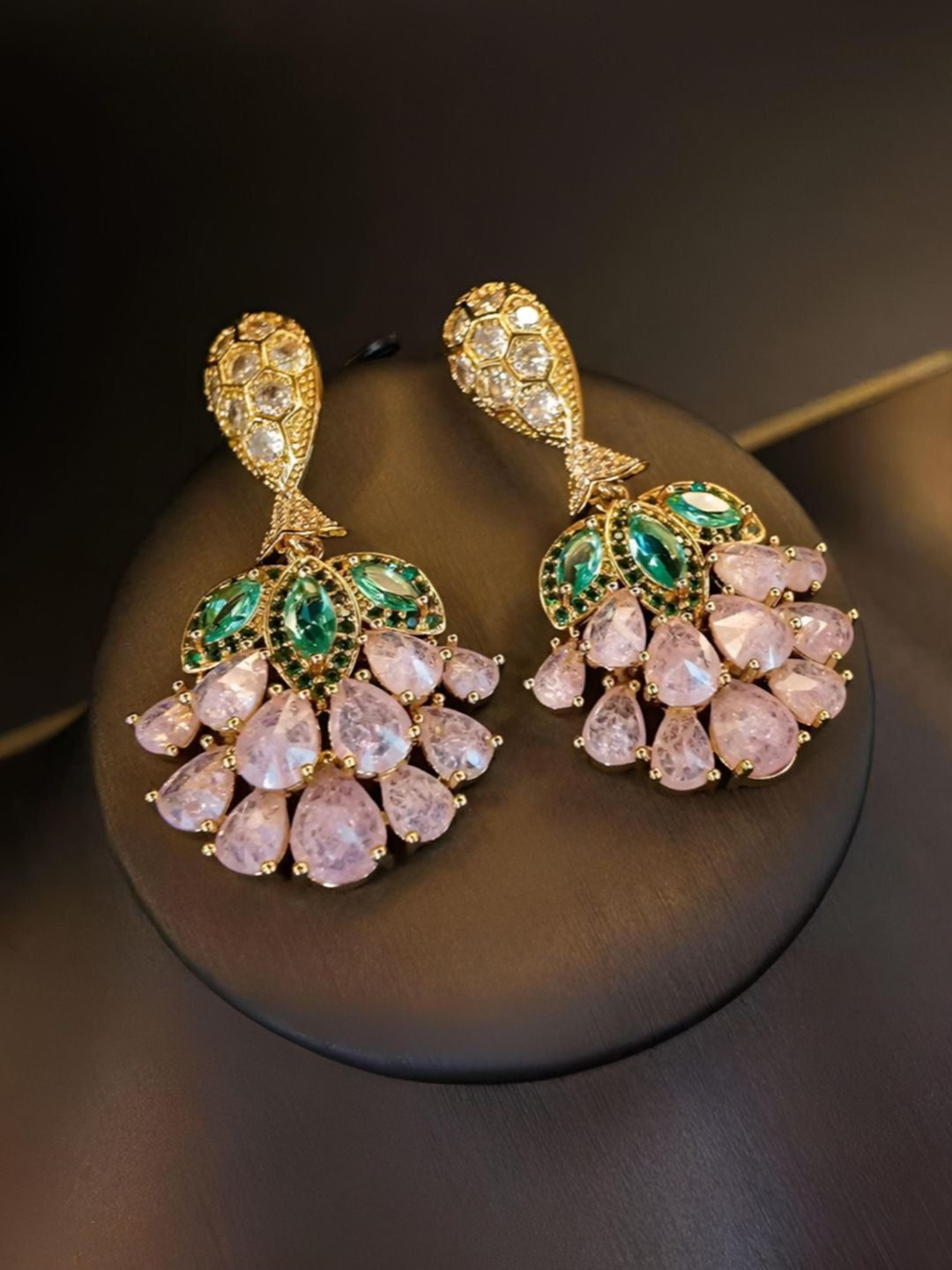 Front view of both gold-plated pink crystal drop earrings displayed on a round black stand