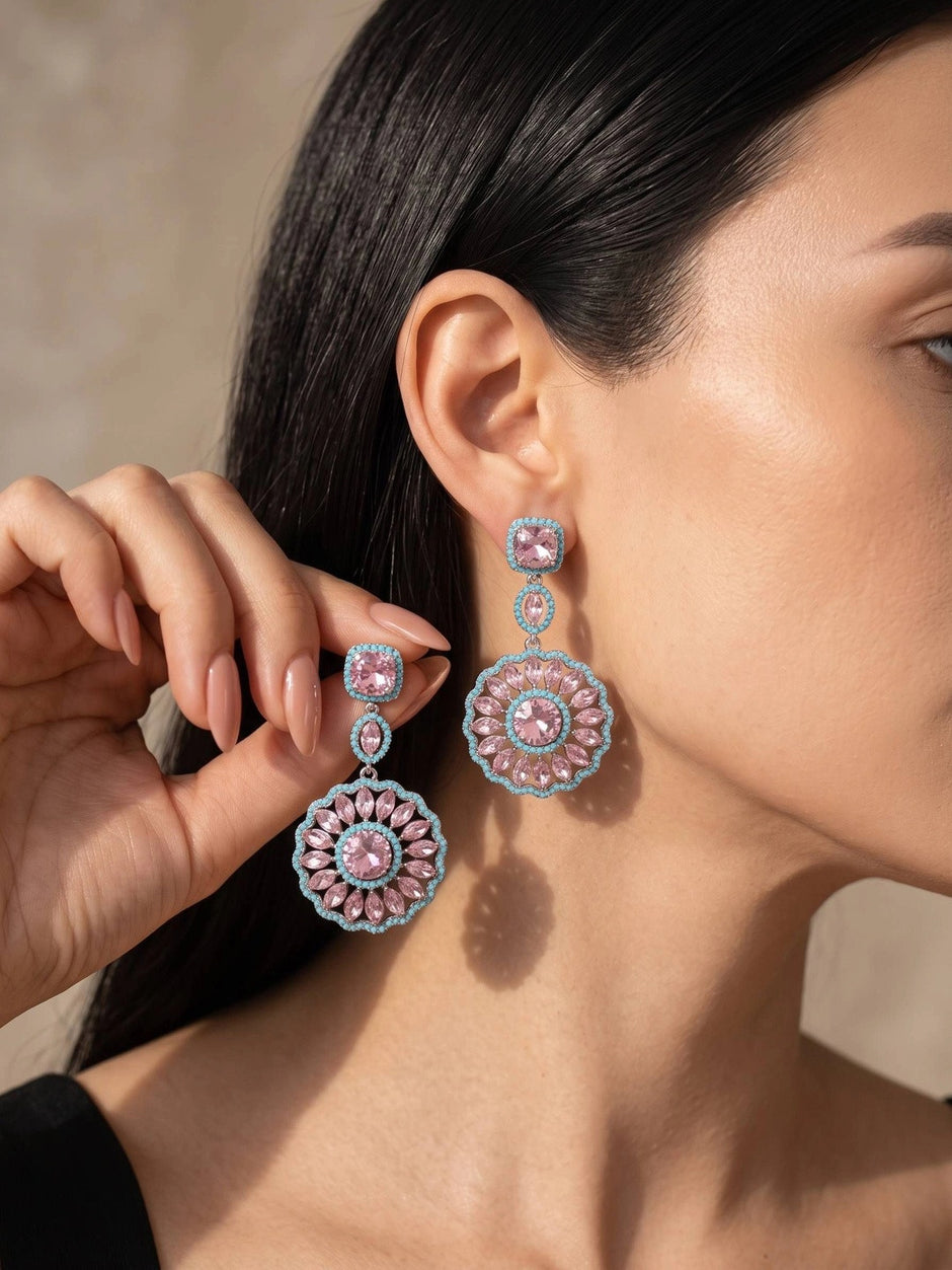 Woman wearing large pink and blue zirconia circular drop earrings against a neutral background