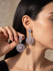 Woman wearing large pink and blue zirconia circular drop earrings against a neutral background