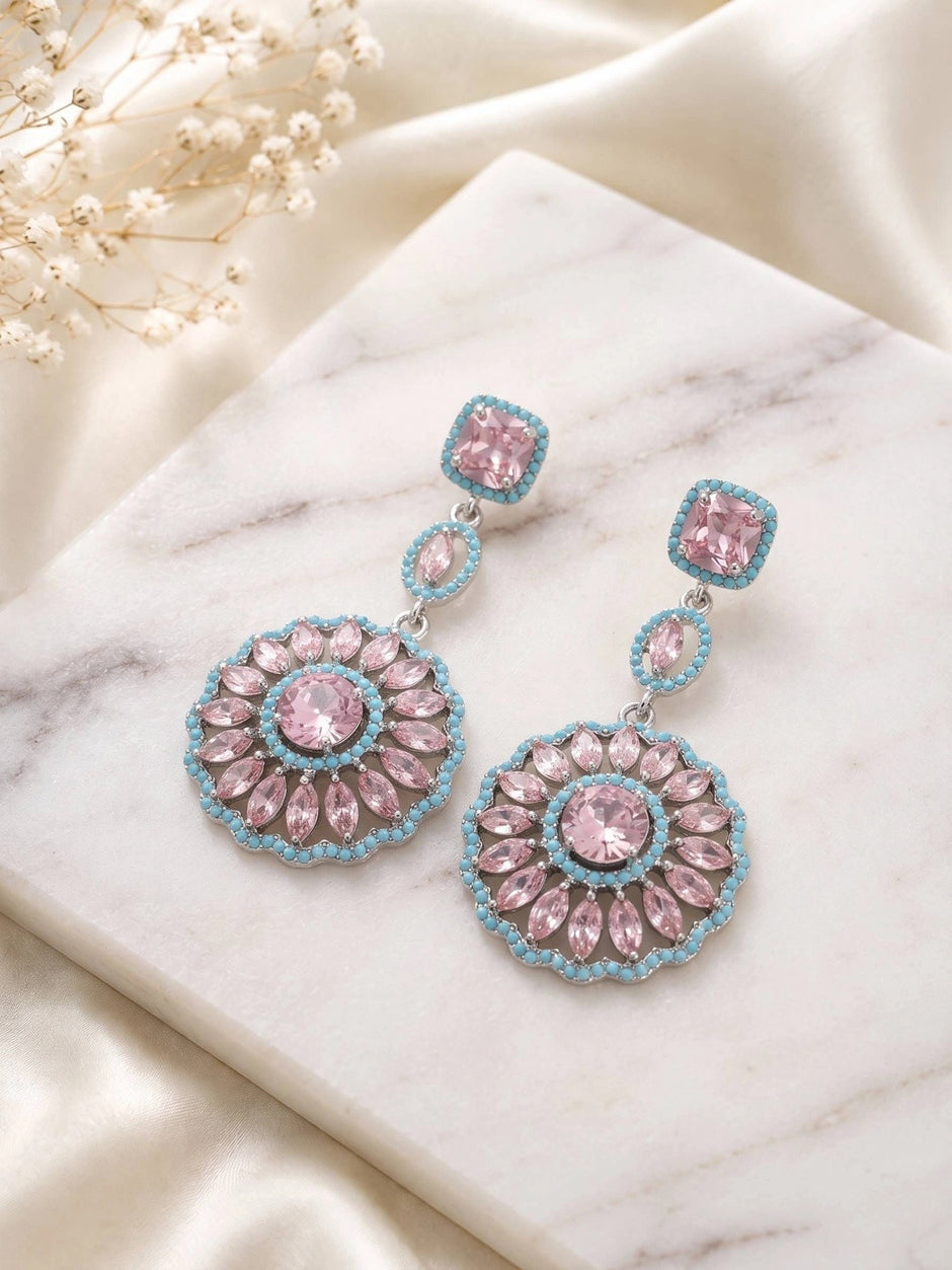 Both earrings laid flat on a white marble surface next to dried white flowers