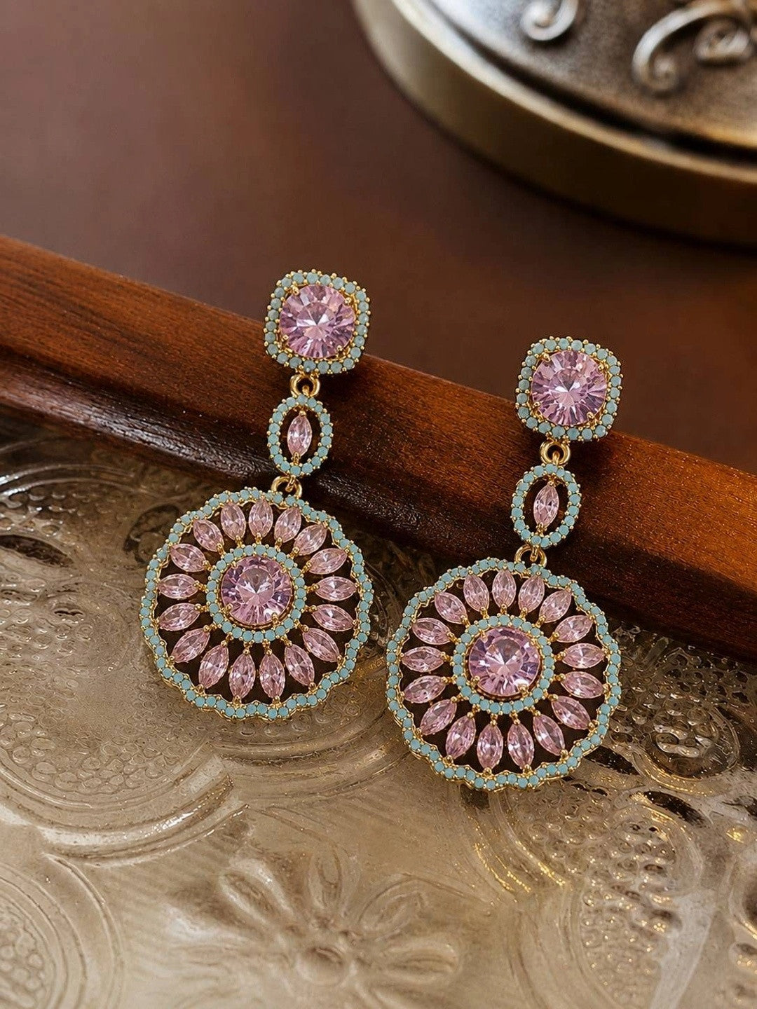 Pair of gold-plated pink crystal circular drop earrings resting on a decorative wooden and metal tray
