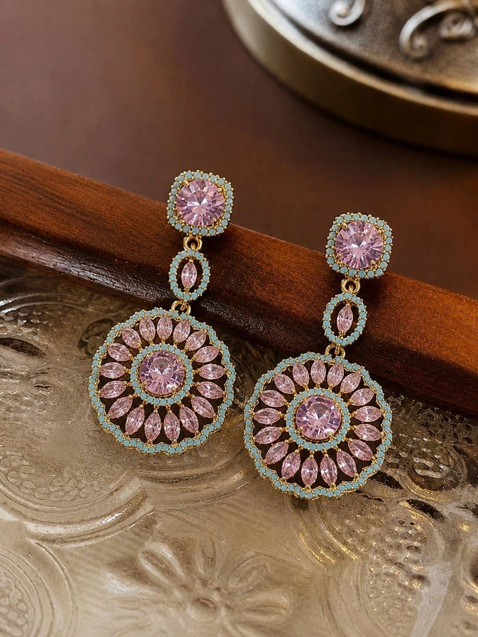 Pair of gold-plated pink crystal circular drop earrings resting on a decorative wooden and metal tray