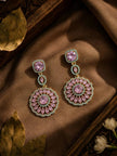 Two gold-plated circular drop earrings with pink stones and turquoise border displayed on golden fabric with dried leaves