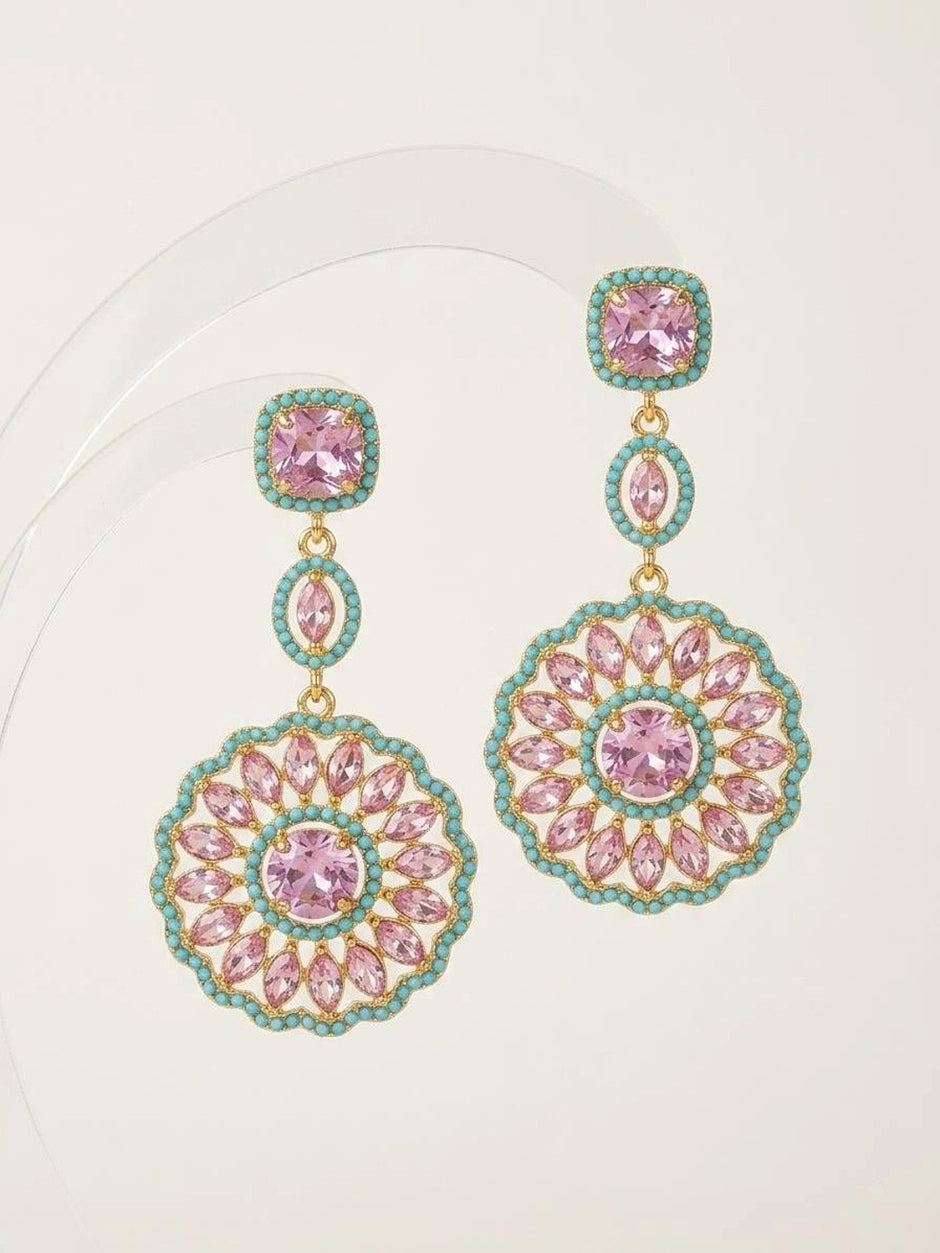 Gold-plated pink and turquoise circular drop earring pair displayed flat against a white curved acrylic surface