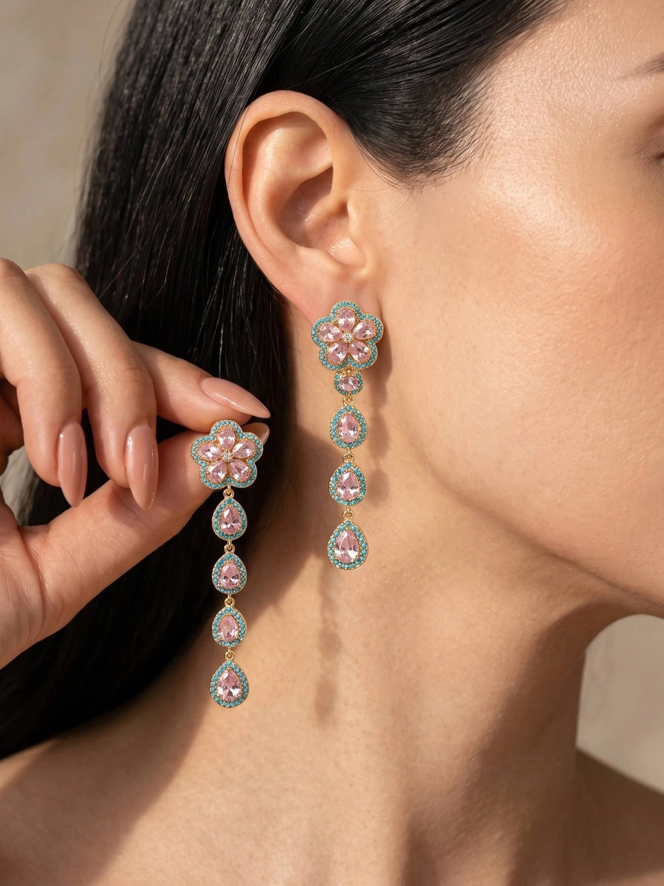 Woman wearing long gold-plated pink crystal floral drop earrings with turquoise pavé border on ear