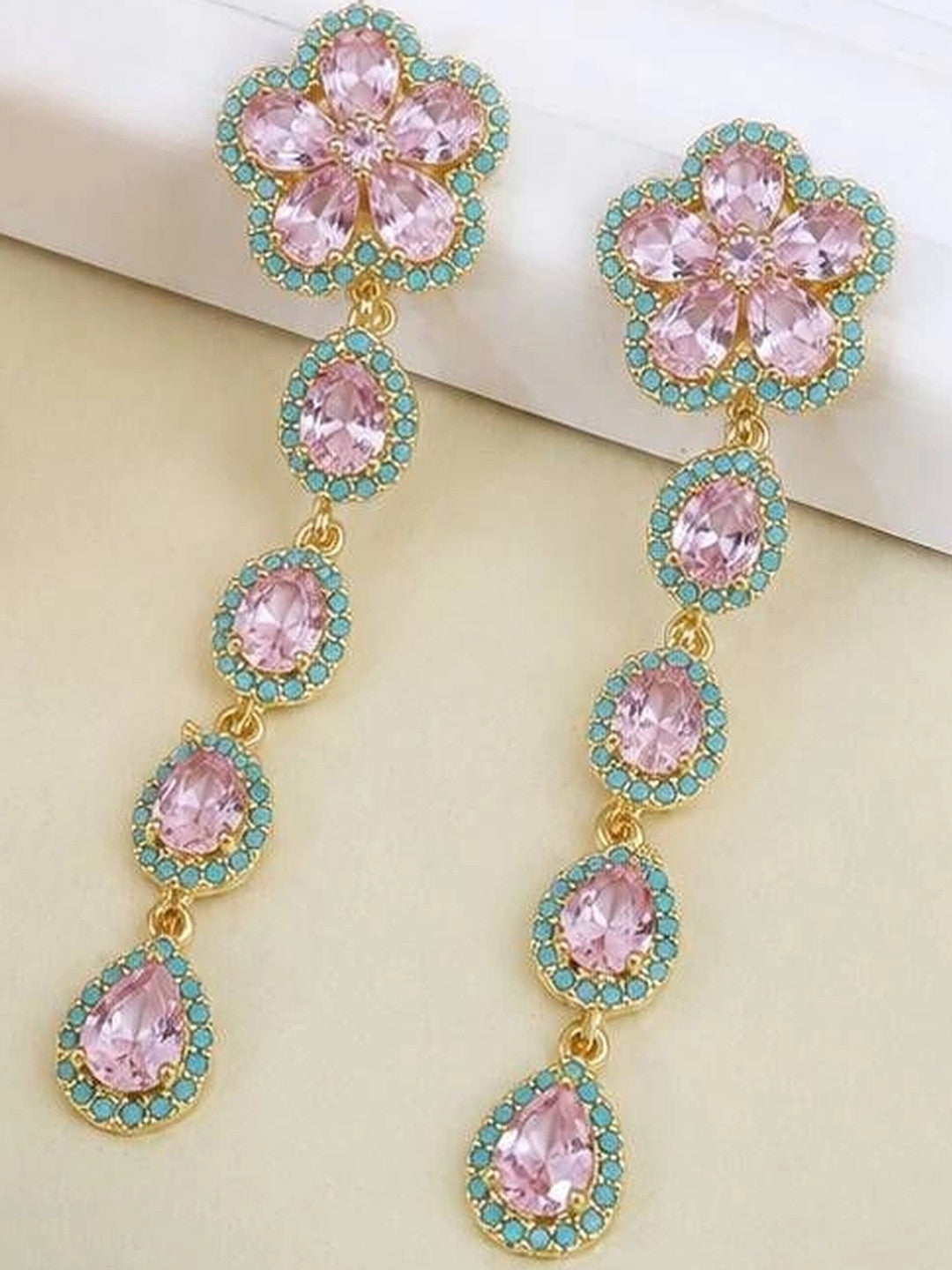 Pair of gold-plated floral drop earrings with pink crystals and turquoise accents on cream surface