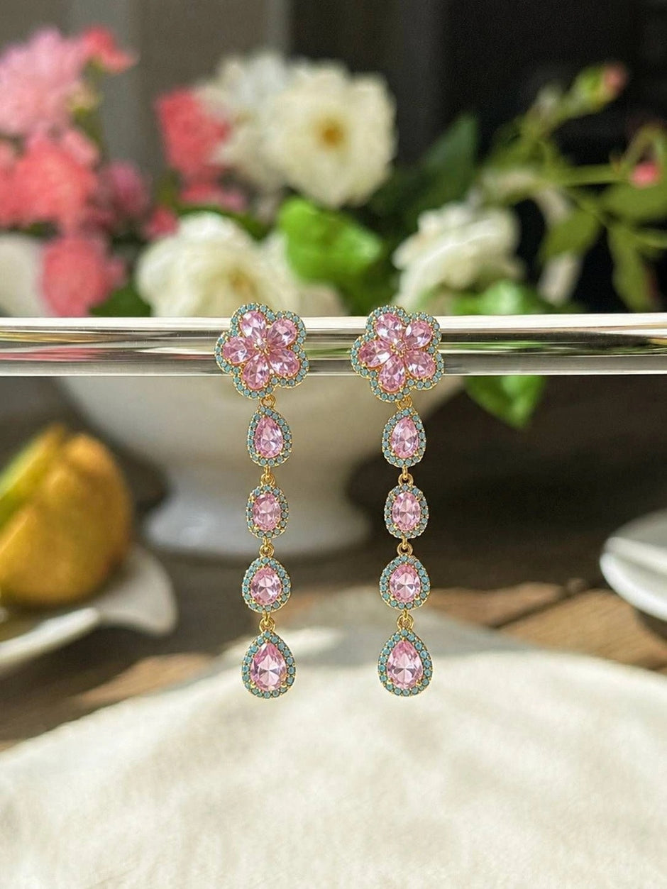 Pink and turquoise floral drop earrings hanging from silver rack with floral background