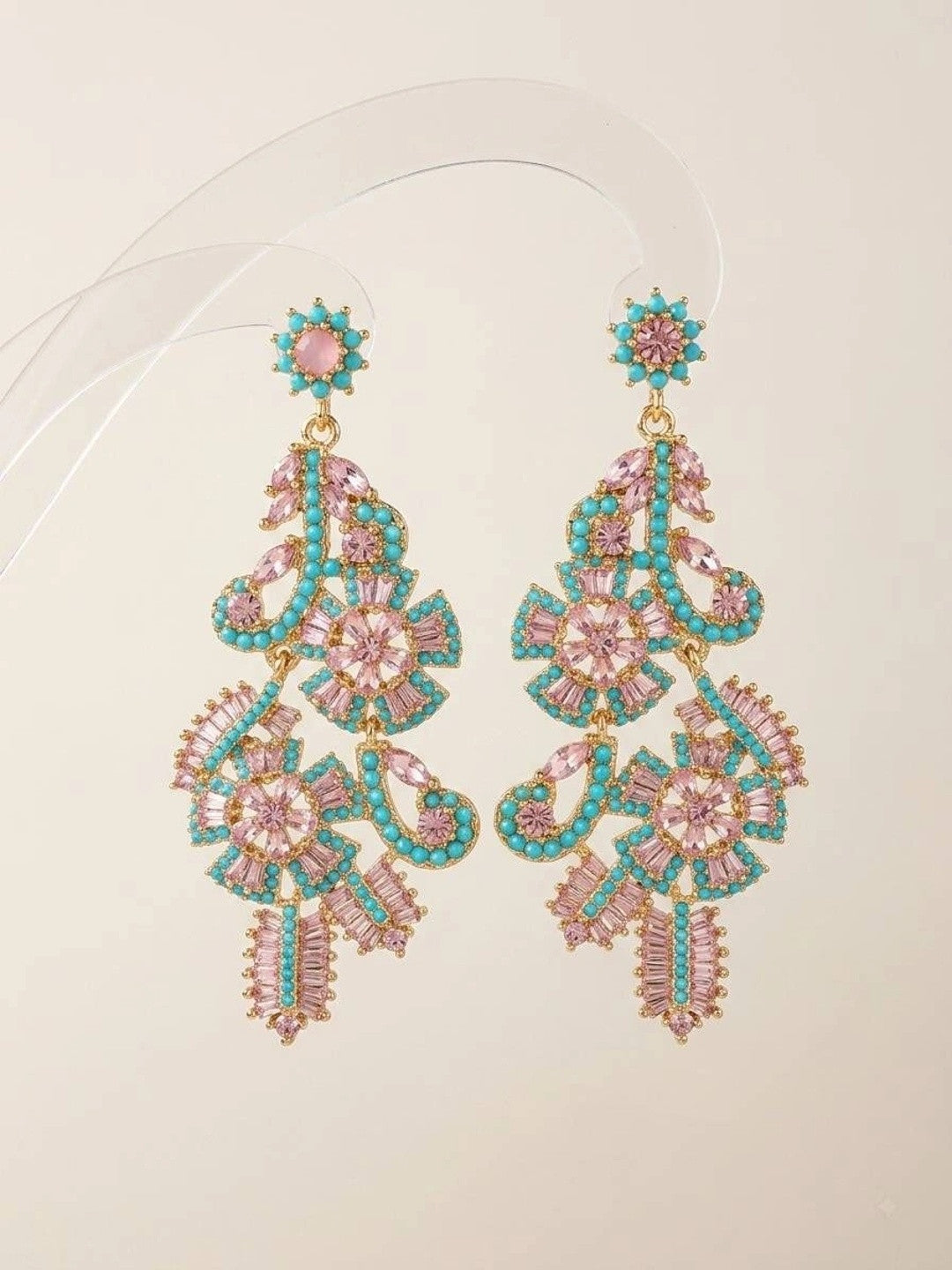 Pair of gold-plated floral chandelier earrings with pink baguette crystals and turquoise beads on clear stand