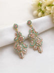 Two gold-plated pink and teal crystal chandelier earrings laid flat on white fabric with flowers