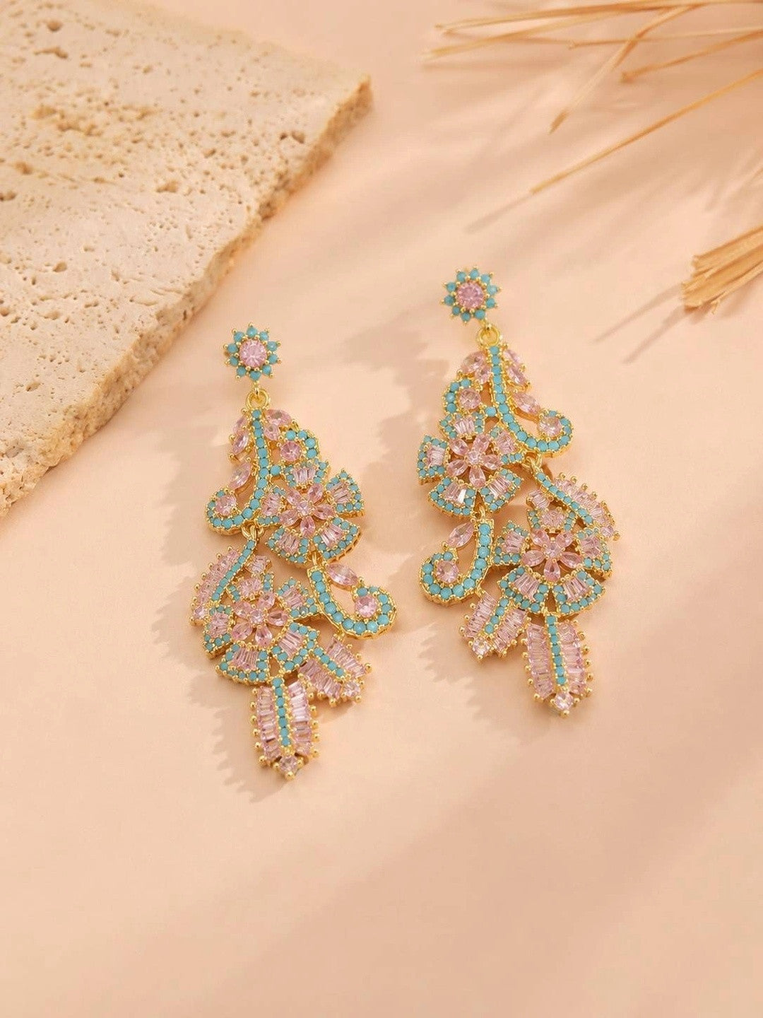 Gold-plated chandelier earrings with pink crystals and turquoise beads placed on textured beige surface