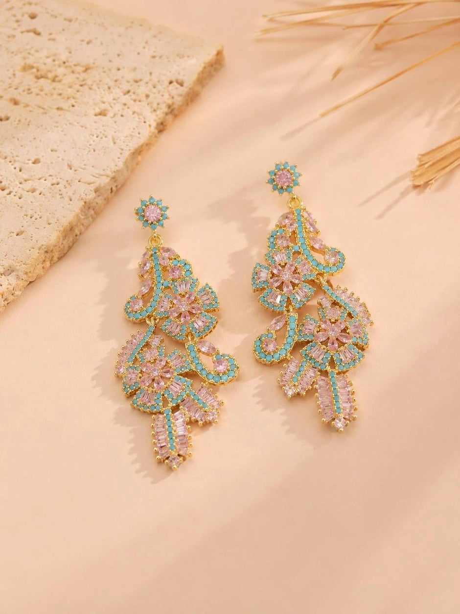 Gold-plated chandelier earrings with pink crystals and turquoise beads placed on textured beige surface