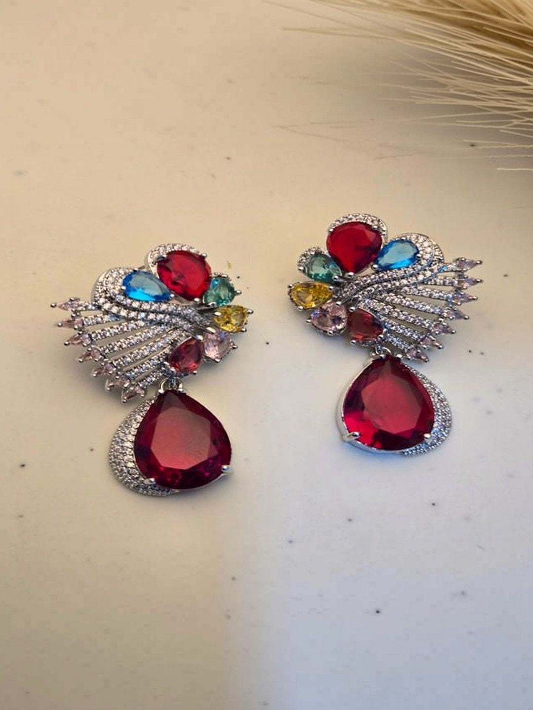 Pair of silver-finish multicolour crystal drop earrings with red teardrop pendant on white surface