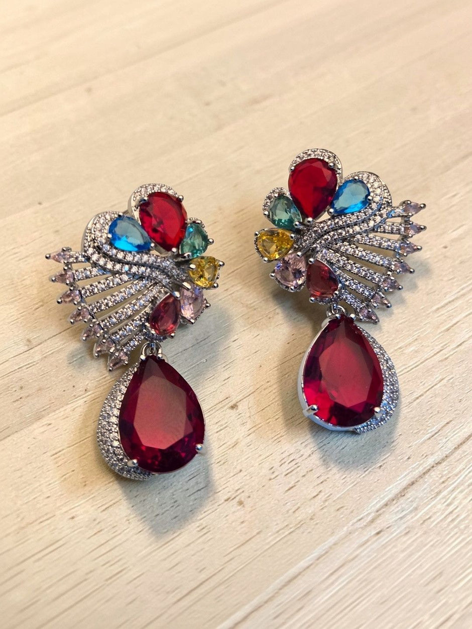 Multicolour crystal fan-top earrings with large red pear-drop pendant displayed on wood surface
