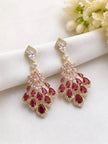 Ruby red and pink cubic zirconia chandelier earrings laid flat on white silk fabric with flowers
