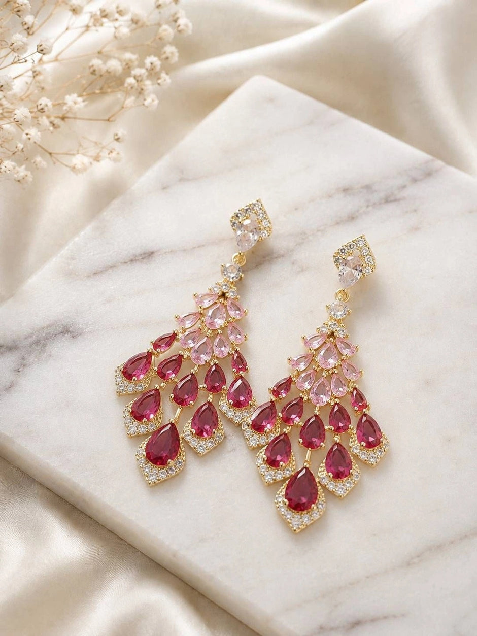 Gold-tone chandelier drop earrings with ruby CZ teardrops displayed on a marble surface