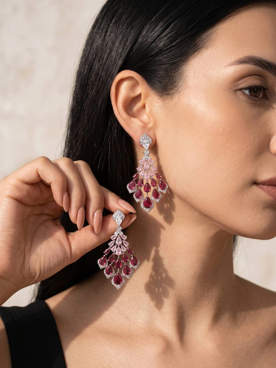 Model wearing long ruby pink CZ chandelier drop earrings, holding second earring up near her ear