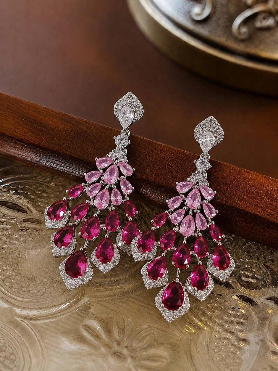 Pair of ruby pink chandelier earrings laid flat on an ornate silver tray against a dark wood surface