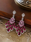 Pair of ruby pink chandelier earrings laid flat on an ornate silver tray against a dark wood surface