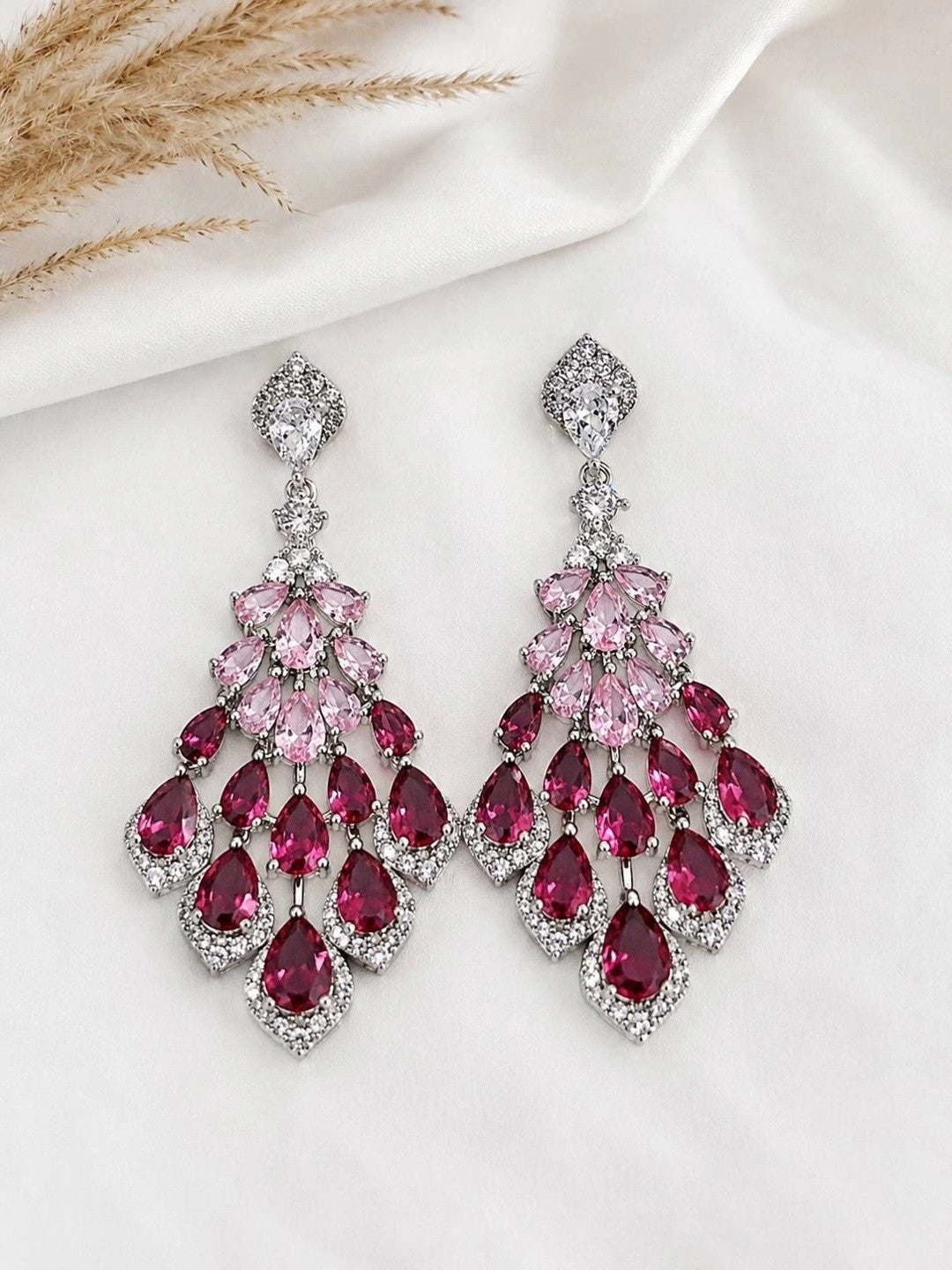 Close-up of ruby and blush pink CZ chandelier earrings placed on a white silk fabric background