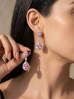 Model wearing long pink CZ teardrop dangle earrings with silver halo setting, holding one earring up close