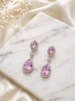 Pink cubic zirconia dangle earrings with silver-toned halo placed on a white marble tile with baby's breath