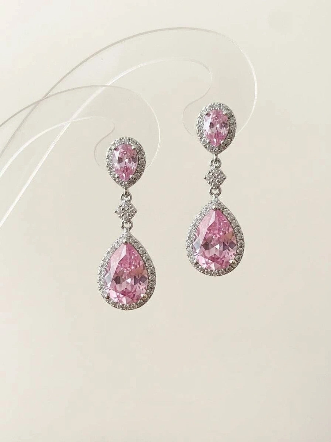 Close-up of pink CZ oval and pear teardrop earrings against a clean off-white background showing full design