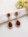 Ruby red gold-plated teardrop earrings laid flat on white fabric with cream florals in background
