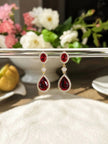 Ruby red teardrop drop earrings suspended from a silver bar with pink and white flowers behind