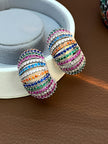 Pair of multicolour zirconia chunky hoops resting against a white jewellery box on a brown leather surface
