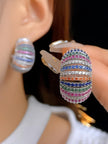 One chunky rainbow zirconia hoop worn on ear while second earring held between fingers showing post back