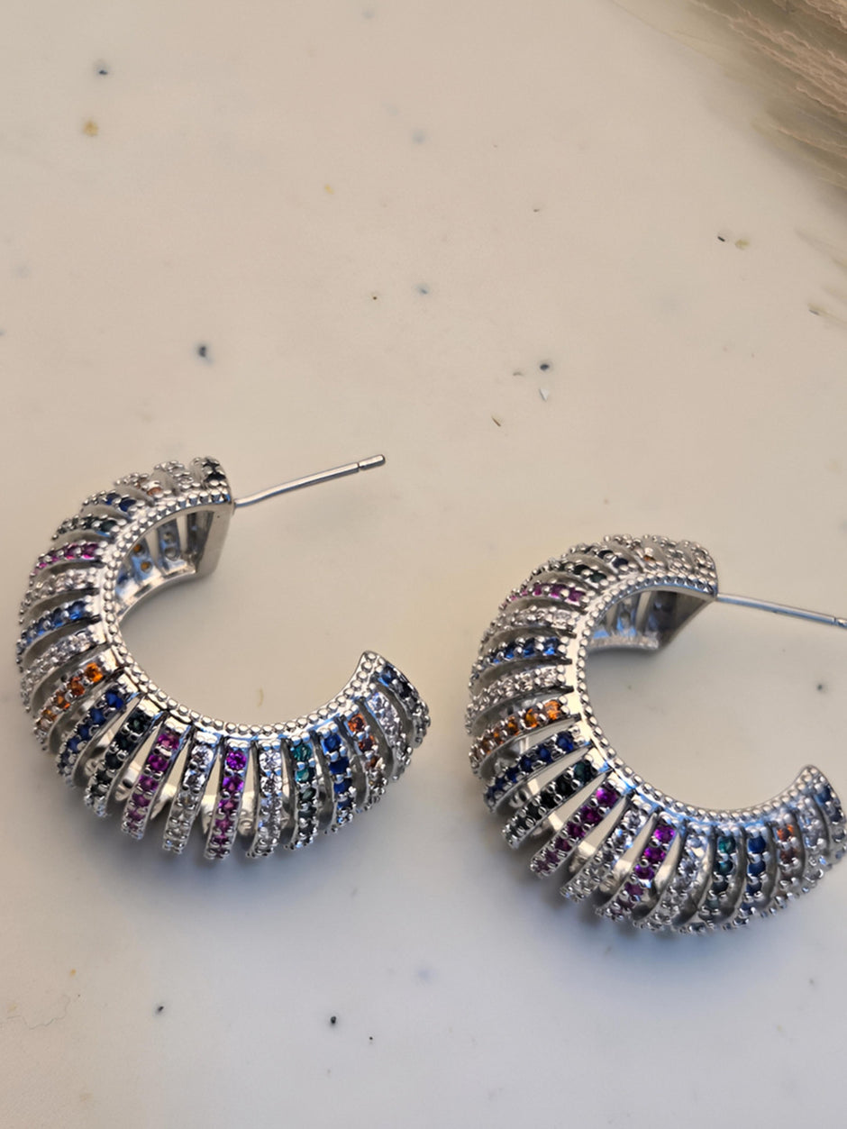 Two chunky multicolour zirconia hoops lying flat on palm displaying vibrant stone rows from above