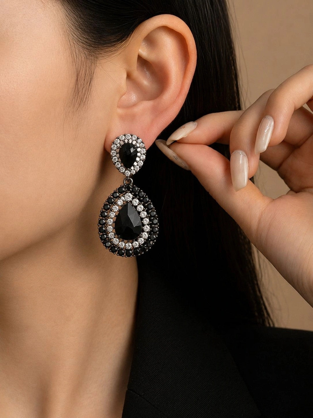 Woman wearing black crystal oxidised teardrop drop earrings against warm beige background