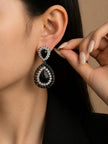 Woman wearing black crystal oxidised teardrop drop earrings against warm beige background