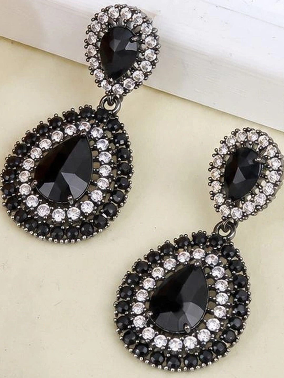 Close-up flat lay of black crystal oxidised drop earring pair on neutral surface
