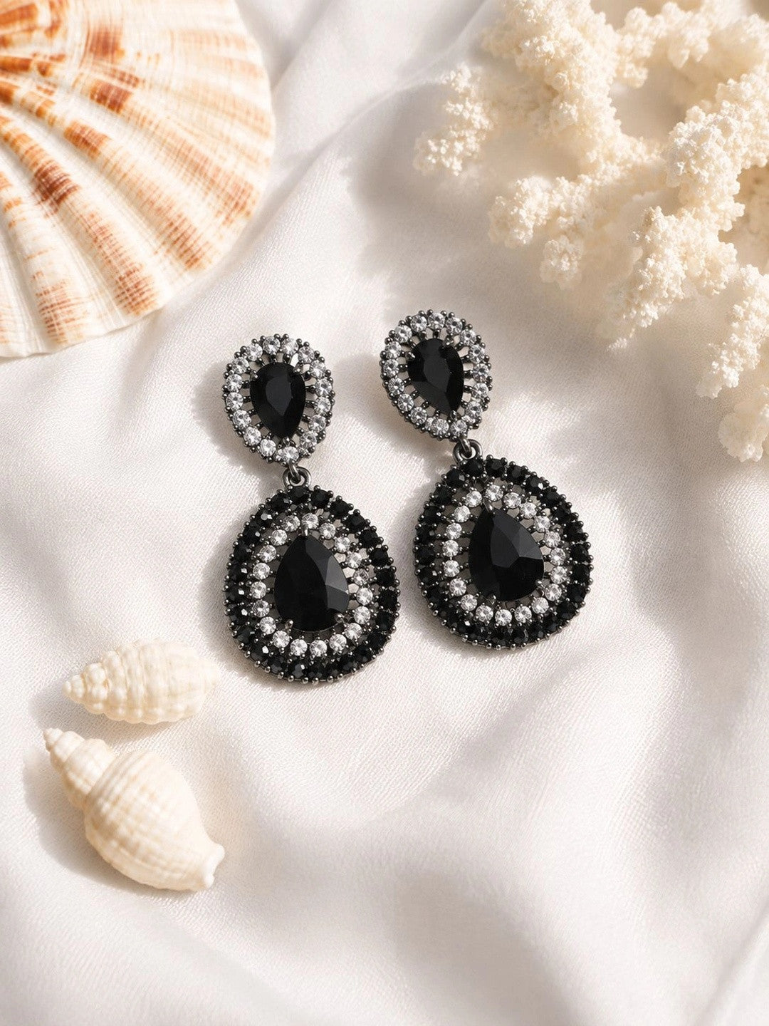 Black crystal oxidised teardrop drop earring pair on white fabric with coral and shell props