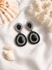 Black crystal oxidised teardrop drop earring pair on white fabric with coral and shell props