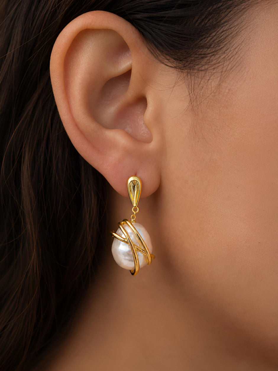 Gold-plated baroque pearl drop earring worn on a model's ear, showing teardrop stud and wrapped pearl pendant