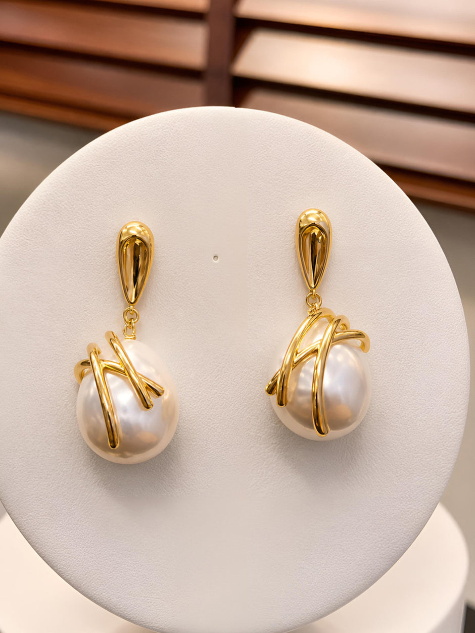 Both gold-plated baroque pearl drop earrings displayed upright on a white jewellery stand against wooden backdrop