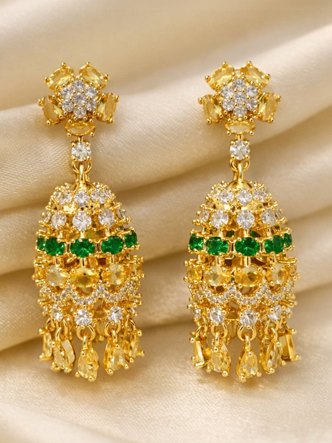 Pair of gold-plated chandelier earrings with white and yellow CZ stones and emerald-green centre row laid on cream silk fabric