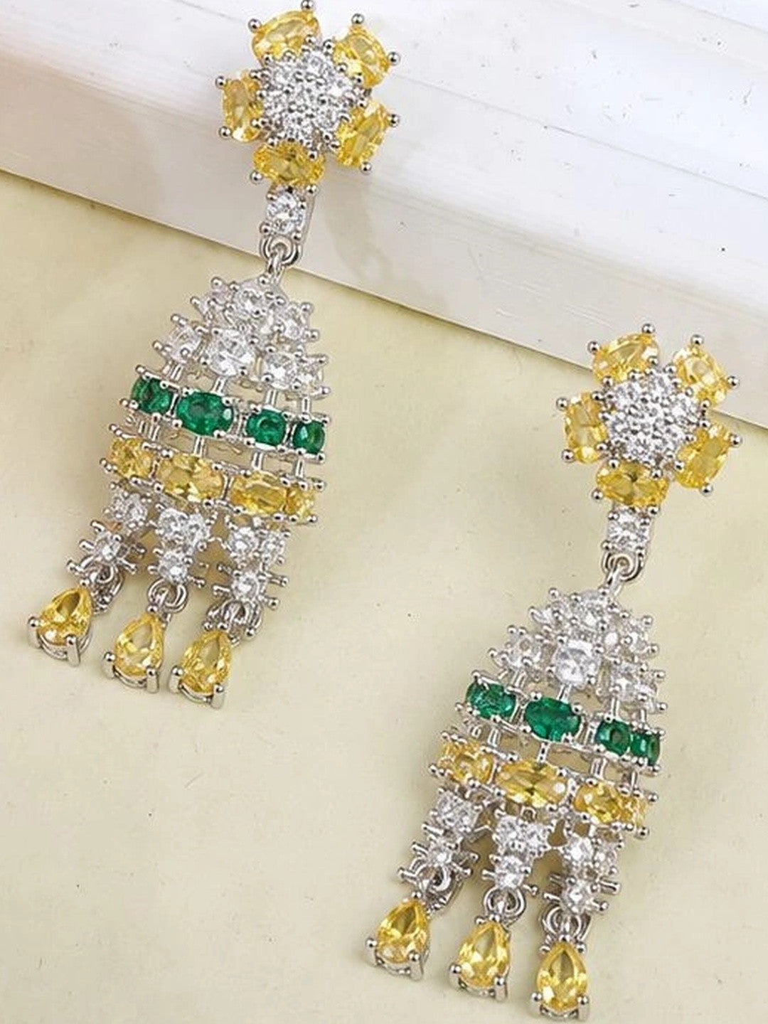 Both chandelier earrings laid flat on white surface showing yellow stud top and emerald green stone row